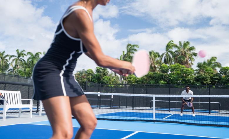 Two aesthetic plastic surgeons playing a pickleball match on an outdoor court at The Boca Raton, with palm trees in the background